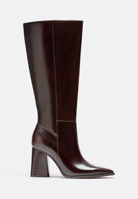 Brązowy skórzany kozak do kolan z wąskim noskiem, blokowym obcasem i widocznymi detalami przeszycia. Gładka faktura z polerowanym wykończeniem.
