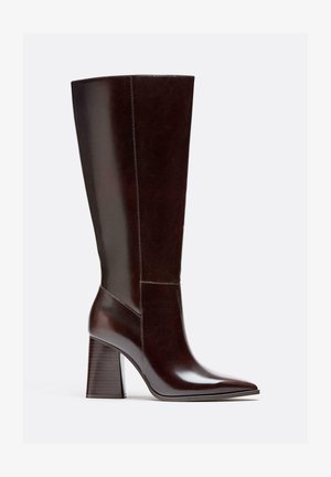 Braune Lederstiefel bis zum Knie mit einer spitzen Zehenform, Blockabsatz und sichtbaren Nahtdetails. Glatte Textur mit glänzender Oberfläche.