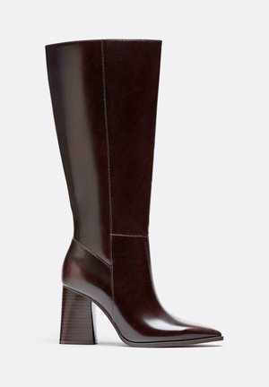 Stivale in pelle marrone alto fino al ginocchio con punta affusolata, tacco a blocco e dettagli di cucitura visibili. Texture liscia con una finitura lucida.