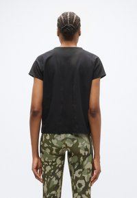 Μαύρο τοπ με κοντά μανίκια, άνετη εφαρμογή και υφασμάτινη υφή, σε συνδυασμό με κολάν σε πράσινο σχέδιο καμουφλάζ με ελαστική μέση.