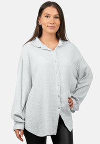 Camicia button-up grigia chiara, con texture, colletto, spalle scese e vestibilità rilassata. Presenta cinque bottoni lungo la parte anteriore e orli laterali a spacco.