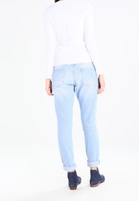 Weißes Langarmoberteil, hellblaue Jeans mit umgeschlagenem Bund und marineblaue Knöchelstiefel, von hinten betrachtet. Weicher Stoff und lockere Passform.