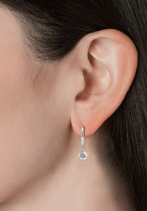 Orecchino a cerchio in argento con design a goccia decorato da un accento di pietra preziosa trasparente. L'orecchino pende appena sotto il lobo dell'orecchio, riflettendo la luce.