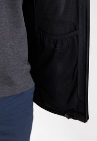 Svart zip-jacka för män med en meshficka på inre vänster sida och en grå tygpanel på det yttre lagret.