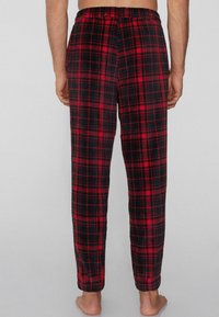 Červené a černé kárované flanelové pyžamové kalhoty s elastickým pasem, zúženým střihem a hladkou texturou, z pohledu zezadu.
