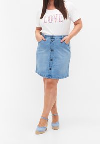 Ljus denim A-linje kjol med framknappar, fickor och en lätt fransad fåll, och kombinerad med en vit grafisk t-shirt och blå espadrillklackar.