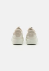 Beige mockaskinn- och lädersneakers med en tjock vit sula; har stoppad krage, logotypdetaljer och slät yta på sidorna.