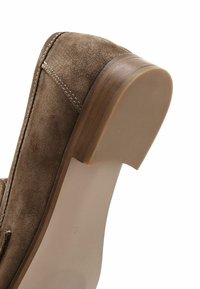 Scarpa in suede marrone con punta arrotondata, cuciture prominenti, tacco in legno e suola in gomma liscia. Il design enfatizza comfort e stabilità.