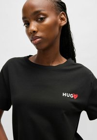 T-shirt in cotone nero con scollatura rotonda, maniche corte e stampa frontale con la scritta "HUG" e un cuore rosso come accentuazione. Texture liscia.