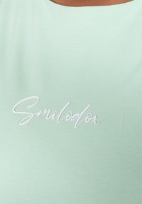 Top sin mangas de color verde menta claro, hecho de una tela suave, que presenta el texto bordado en blanco "Smilodox" en la parte frontal.