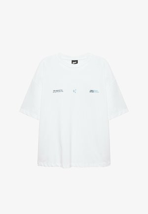 T-shirt blanc oversize à manches courtes avec petit texte "shaped by the future" à gauche et "random evolution" sur la partie droite de la poitrine.