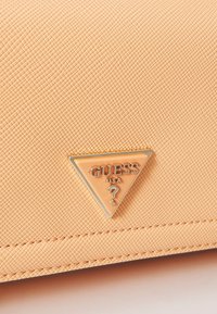 Portafoglio in pelle sintetica color pesco con superficie testurizzata, caratterizzato da un accento triangolare del logo "GUESS" in oro e argento.