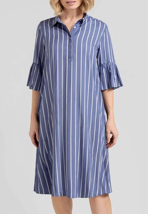 Donna che indossa un vestito blu fino al ginocchio con righe verticali bianche e maniche al gomito con dettagli a volant.