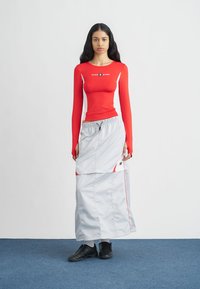 Red long-sleeve top with white accents and logo, paired with a gray, lightweight, drawstring maxi skirt featuring red detailing. Black footwear.