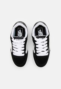 Schwarze Wildledersneaker mit weißen Schnürsenkeln, ausgestattet mit einem weißen Seitenstreifen und einem schwarzen Logo auf der Zunge. Flache Gummisohle.