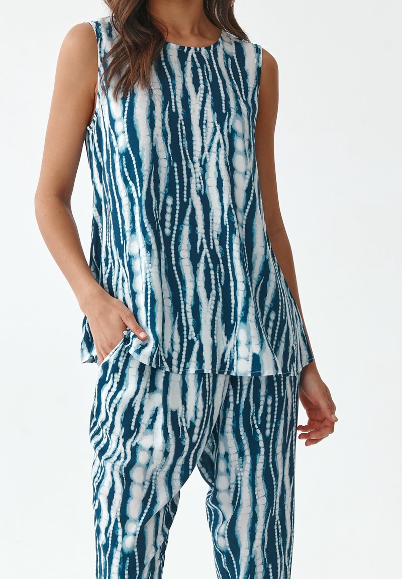 Haut sans manches en bleu sarcelle et blanc avec un design fluide, doté d'un col rond et de motifs semblables à des rayures verticales.