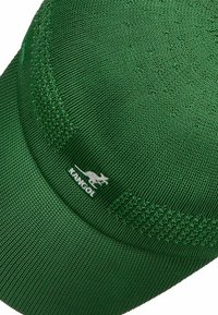 Green cap made of textured fabric, featuring a rounded crown and a flat brim. Includes a white logo with a kangaroo.