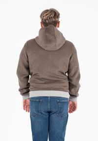 Felpa con cappuccio marrone e polsini e orlo grigi a coste, caratterizzata da una vestibilità rilassata e da una consistenza morbida. Indossata con jeans blu.