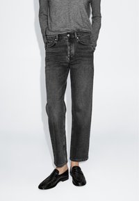 Jeans in denim nero con taglio dritto, dotati di un classico design a cinque tasche e dettagli cuciti, abbinati a mocassini neri texturizzati.