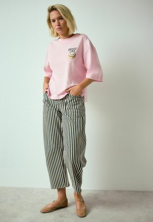 Light pink oversized t-shirt with "SWEET LIKE" text and graphic; paired with high-waisted striped trousers in beige and dark blue.