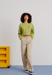 Khaki wide-leg pants with a cropped, light green sweatshirt featuring a logo design. The outfit is paired with black and white sneakers.