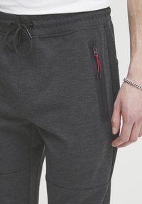 Joggers grises texturizados con una cinturilla ajustable, que cuentan con un bolsillo con cremallera con acentos rojos y un corte plano y casual.