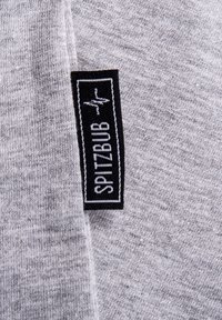 Grauer Stoff mit einer glatten Textur, der ein schwarzes Etikett mit weißem Text aufweist. Das Etikett ist horizontal entlang der Stoffkante platziert.