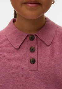 Barn som har på sig en strukturerad rosafärgad stickad tröja med spetsig krage och tre stora bruna knappar framtill.