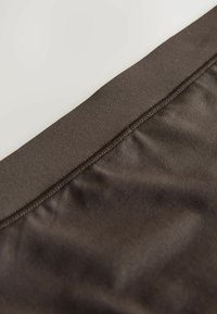 Smeđi tekstil s glatkom teksturom, s širokim elastičnim strukom i detaljnim šavom uz rub.