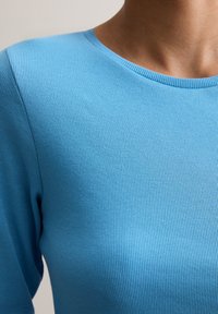 Blauwe geribbelde langekoestop met een ronde halslijn, gemaakt van een zachte, ademende stof, met een gestructureerd oppervlak en een getailleerd ontwerp.