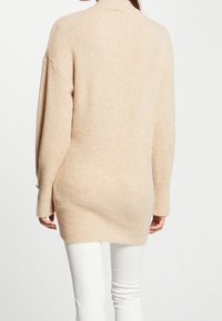 Pull beige à manches longues avec un col montant, un ourlet côtelé et une coupe légèrement oversize, fabriqué en tissu doux et texturé.