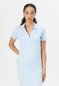 Lyseblå polo-kjole med korte ermer, V-hals og subtil hvit kant. Har en liten logo på brystet og en tettsittende design.
