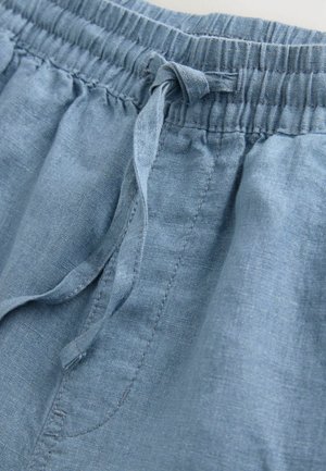 Světle modrá lněná tkanina s elastickým pasem a šňůrkou. Vyznačuje se měkkou strukturou a jemným leskem. Detailní záběr ukazující detaily prošívání.