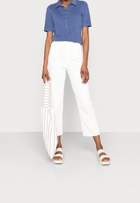 Camisa polo de algodón en azul con tapeta de botones, combinada con pantalones recortados blancos. Lleva un bolso de rayas y sandalias beige.