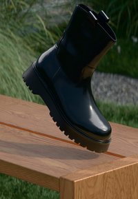 Schwarze Knöchelboots mit glänzender Oberfläche, dicker Gummisohle und minimalistischem Design. Mit einer Zuglasche oben für einfaches Anziehen.