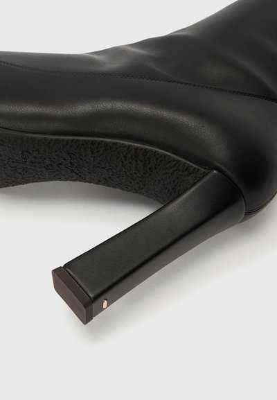 Melna ādas augstpapēžu zābaki ar teksturētu zoli, kvadrātveida papēdi un smalku zelta akcentu pie papēža pamatnes. Gluda apdare ar šuvju detaļām.