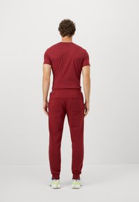 Burgundi pamut póló és hozzá illő melegítőnadrág. A póló kerek nyakú; a melegítőnadrág oldalzsebekkel és keskenyített lábakkal rendelkezik. Fehér sportcipők is included.