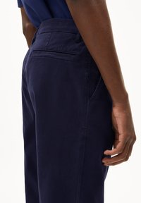 Donkerblauwe chinos met een gladde textuur, voorzien van een achterzak en een zijzak. Eenvoudig ontwerp, rechte pasvorm.