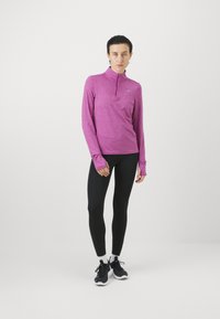 Dug dugih rukava, majica s poluzipom, tijesnog kroja od heathered ružičaste tkanine; nosi se s crnim tajicama i sportskim crnim tenisicama. Glatka tekstura, jednostavan dizajn.