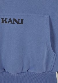 Kék pulóver bordás mandzsettákkal és aljjal, elülső zsebbel, és a mellkasán fekete betűkkel a "KANI" felirattal.