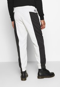 Nohavice v černobílé barvě, s elastickým pasem, zúženým střihem a kontrastními postranními panely. Tkanina vypadá lehká a hladká.