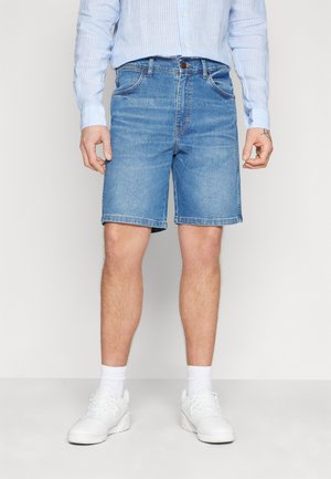 Shorts in denim blu chiaro, vestibilità casual, con cinque tasche, orlo cucito e chiusura con bottone. Indossati con sneakers bianche e calzini alla caviglia.