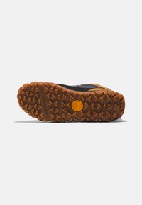 Suela de goma con un patrón de agarre texturizado, de color marrón con tacos triangulares y un logo circular naranja en el centro.