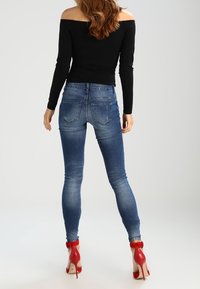 Jeans ajustados en denim de lavado medio con una textura suave, combinados con zapatos de tacón rojo con correas en el tobillo y un diseño de punta afilada.