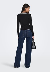 Pull noir côtelé avec un col blanc, associé à un jean large bleu foncé avec deux poches arrière. Complété par un sac à main noir.