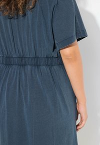 Sininen mekko, jossa on joustava vyötärö, lyhyet hihat ja tekstiili, jossa on hienovaraisia raitoja, näkyy takaa.