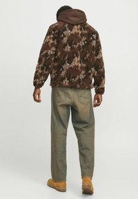 Brown patterned fleece jacket layered over a brown hoodie, paired with light green jeans and tan boots. Soft texture, relaxed fit.