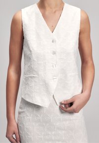 White, sleeveless vest with a v-neck, textured leaf pattern, five buttons, and two front pockets. Slightly cropped design.