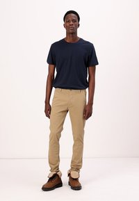 Navy crew-neck t-shirt paired with beige straight-leg pants. The model wears brown boots with tan accents and visible laces.