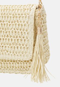 Wiklinowa torebka z plecionego słomy w jasnożółtym kolorze, o fakturowanej powierzchni, z zapięciem w kolorze złotym i długą ozdobną frędzlą.